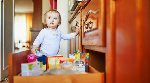 Toddler standing by an open kitchen drawer filled with items, exploring.