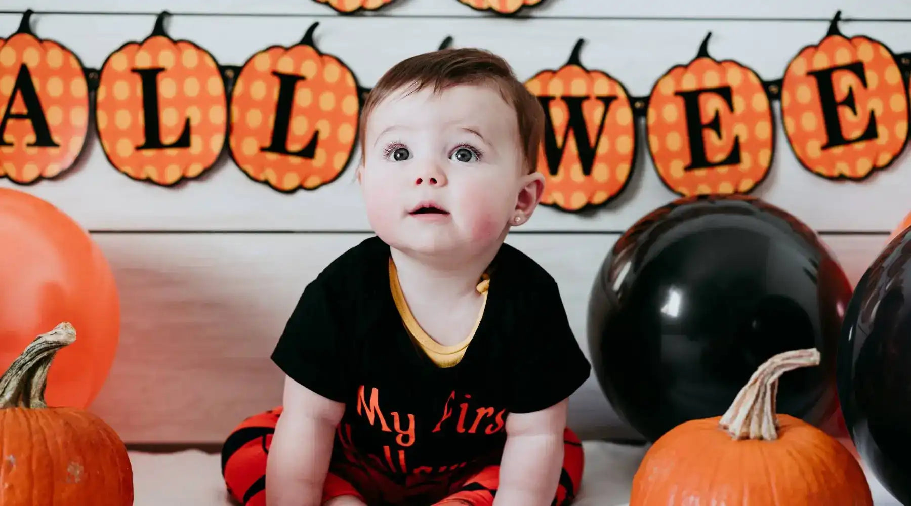 Baby wearing “My First Halloween” outfit sits among pumpkins and festive decor, celebrating baby milestones.