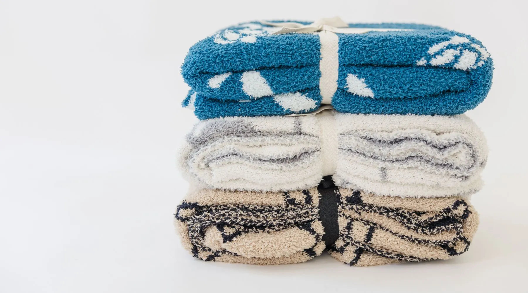 A stack of soft baby blankets in blue, gray, and beige with a cute design, tied together with ribbons.