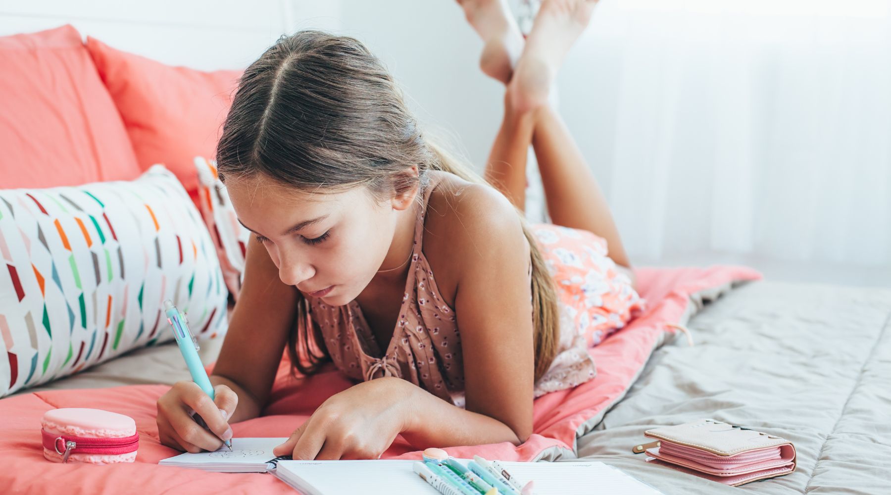 pre-teen girl writing on her bed