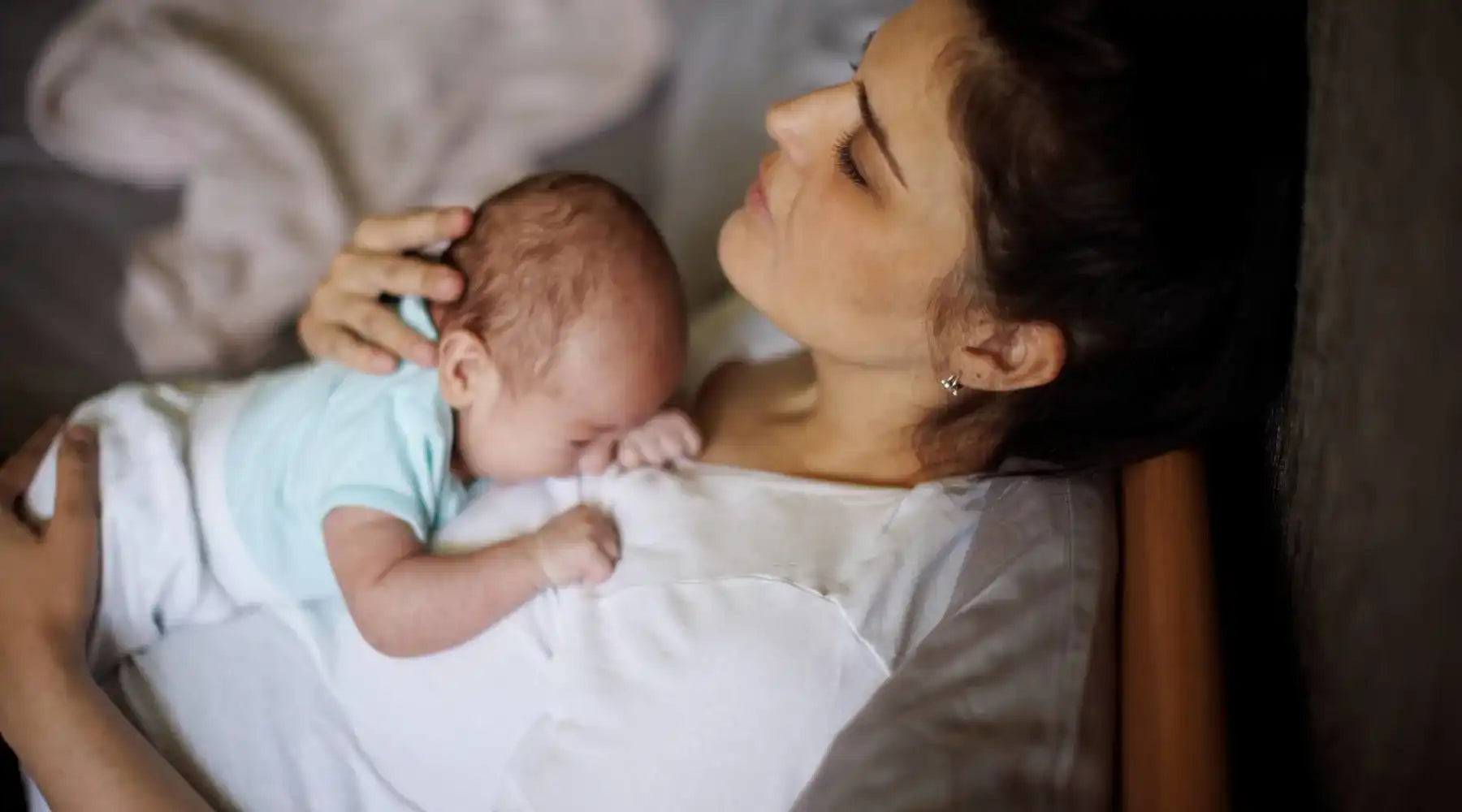 Mother resting with newborn baby lying on her chest, both appearing calm and peaceful.