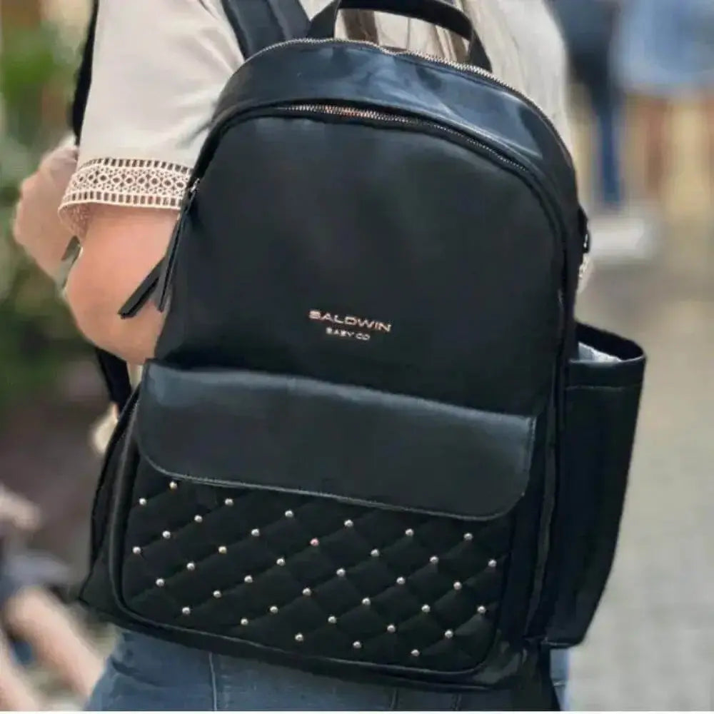 Woman walking with black leather backpack diaper bag with rose gold studs quilted on front pocket  