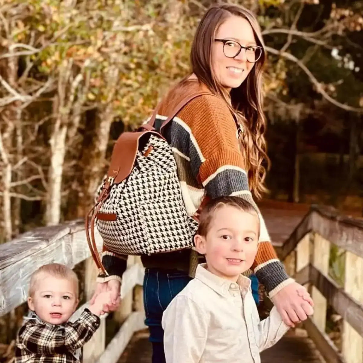 Woman wearing houndstooth and brown leather backpack diaper bag with holding hands with two young boys