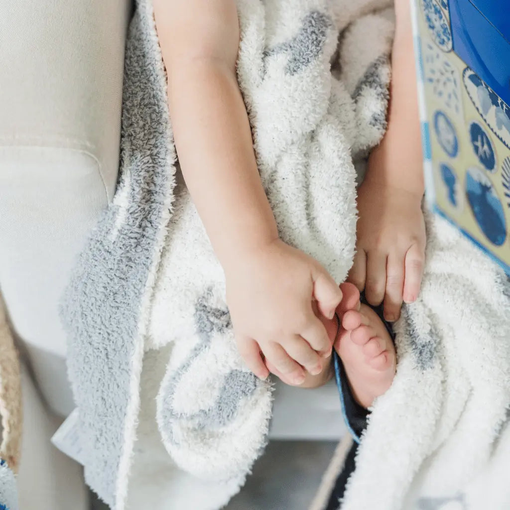 white blanket with grey herons in the lap of a child with their feet peeking out