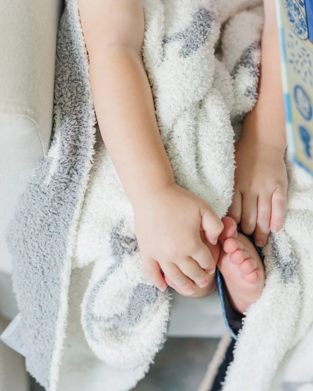 white blanket with grey herons in the lap of a child with their feet peeking out