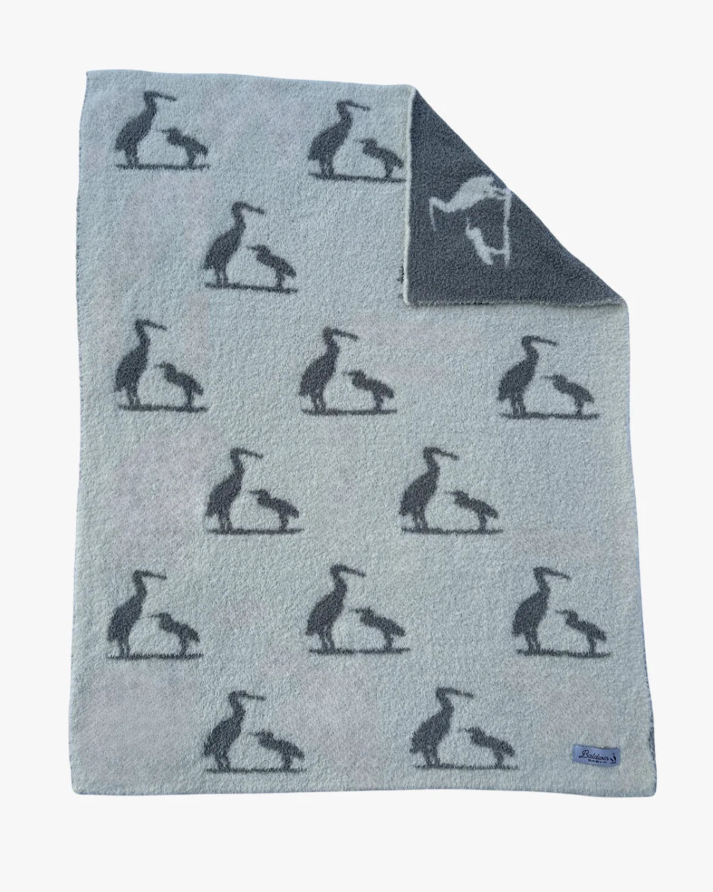 Creamy white with a gray mother and baby heron silhouette pattern blanket laid flat. A corner is folded over showing the other side has a reversed color pattern