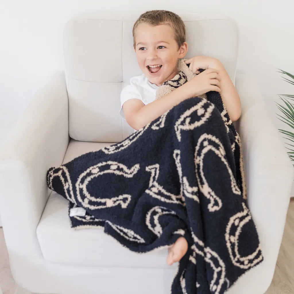 smiling boy sitting in a white chair with a black blanket with tan horseshoes in his lap