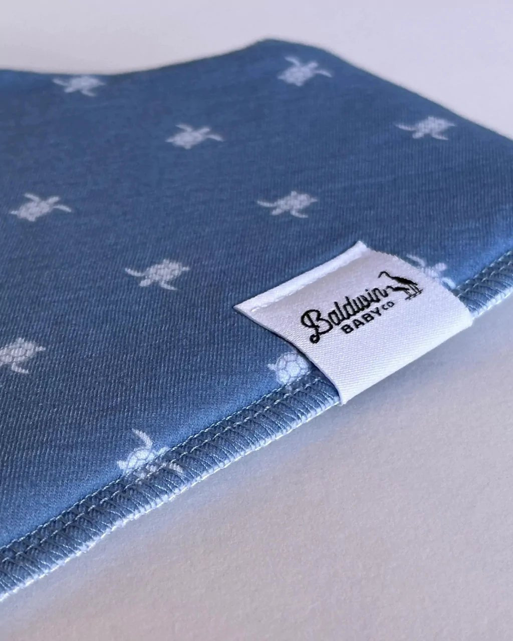 Close up of navy with small white sea turtle pattern bandana bib with a white Baldwin Baby Company logo tag