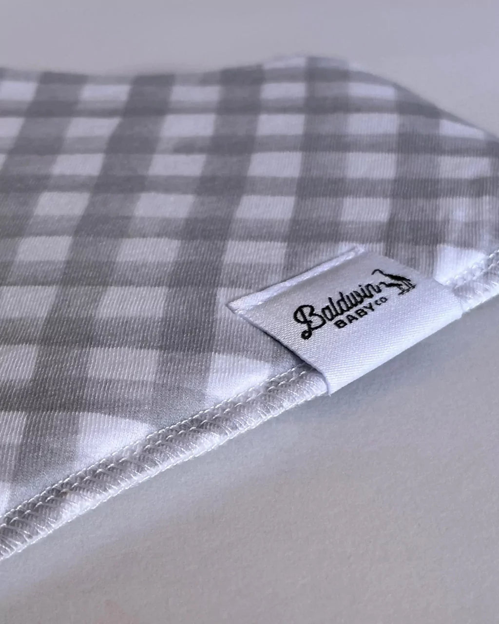 Close up of a timeless gray and white checkered pattern bandana bib with a white Baldwin Baby Company logo tag