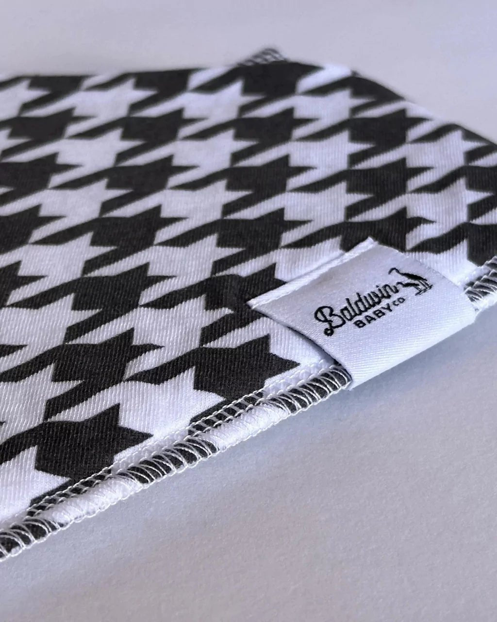 Close up of a traditional white and black houndstooth pattern bandana bib with a white Baldwin Baby Company logo tag