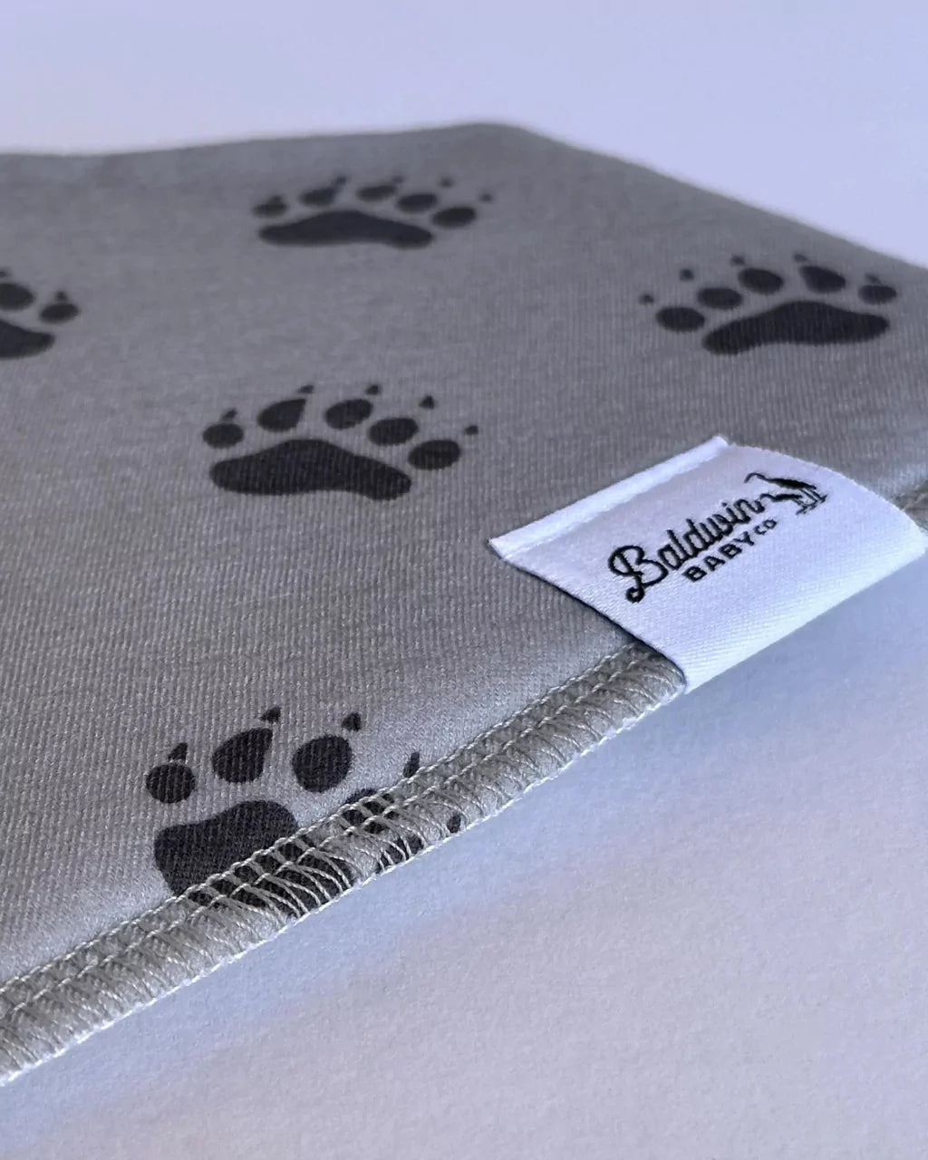 Close up of gray with black bear paw track pattern bandana bib with a white Baldwin Baby Company logo tag