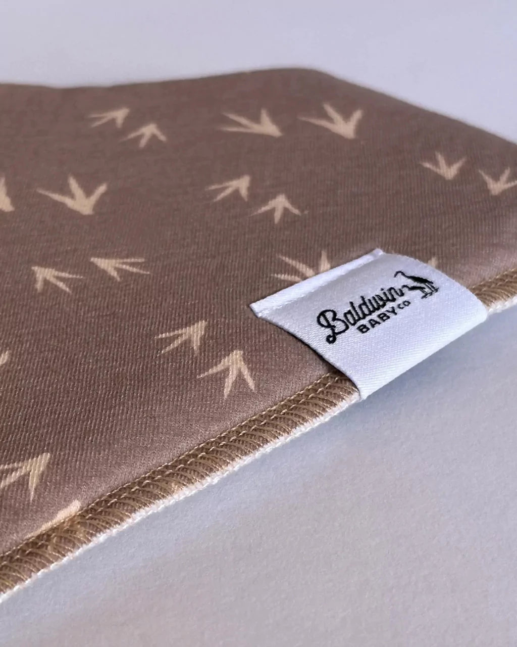 Close up of brown with tan turkey track pattern bandana bib with a white Baldwin Baby Company logo tag