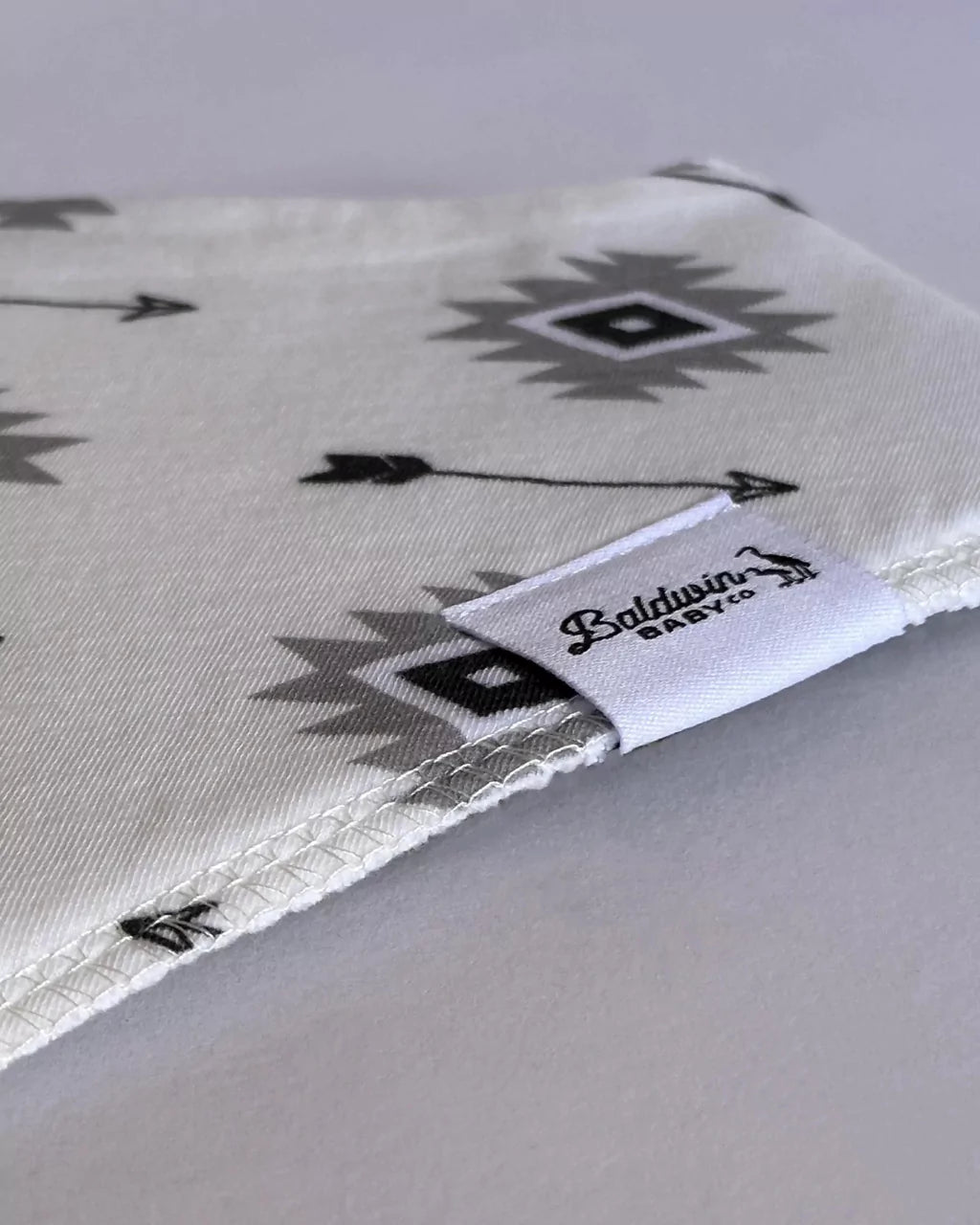 Close up of a creamy white and black arrow pattern bandana bib with a white Baldwin Baby Company logo tag