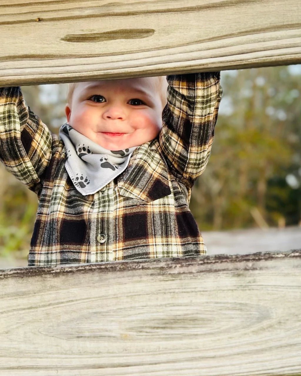 Toddler boy wearing a gray with black bear foot print pattern bandana bib by Baldwin Baby Co