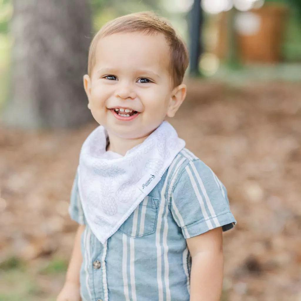 Toddler boy wearing a white with blue, pink, and green pineapples pattern bandana bib by Baldwin Baby Co
