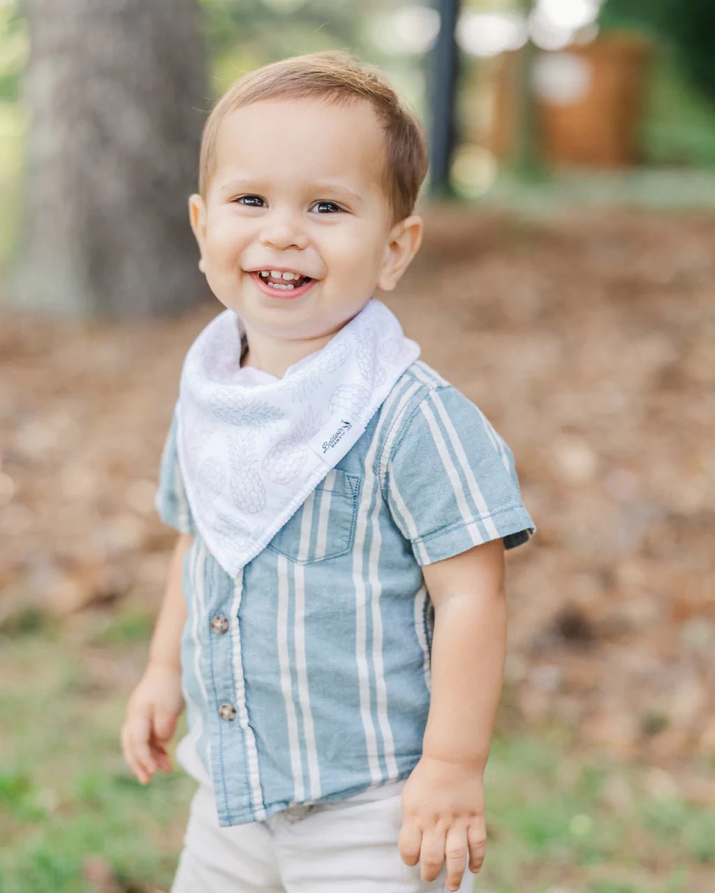 Toddler boy wearing a white with blue, pink, and green pineapples pattern bandana bib by Baldwin Baby Co