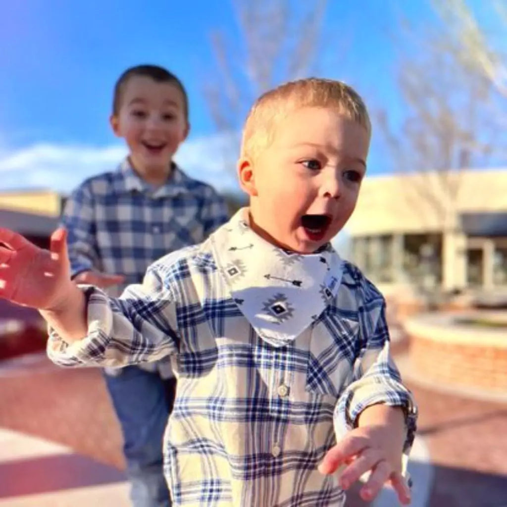 two boys playing with one boy wearing creamy white and black arrow pattern bandana bib by Baldwin Baby Co