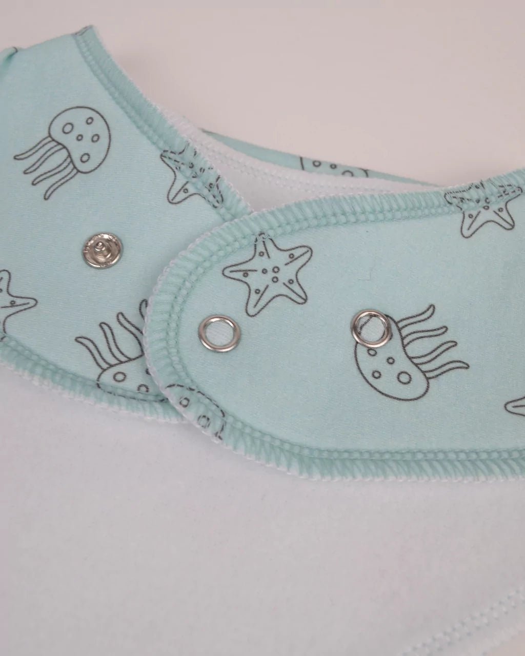 Close-up of snaps on the back of a light blue with starfish and jellyfish pattern bandana bib