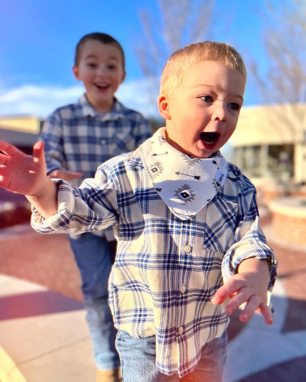 two boys playing with one boy wearing creamy white and black arrow pattern bandana bib by Baldwin Baby Co