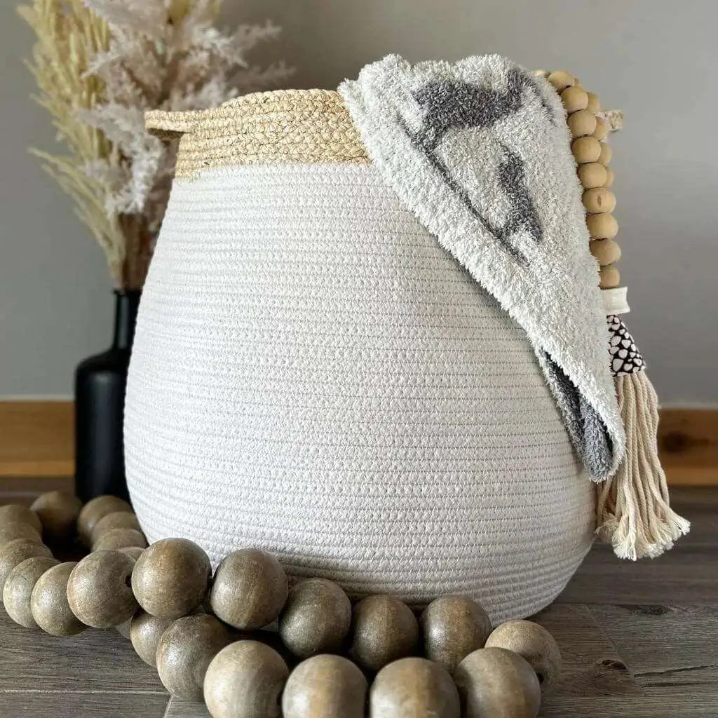 white bell shaped rope basket with corn husk details and handles styled with a blanket and large wooden beads