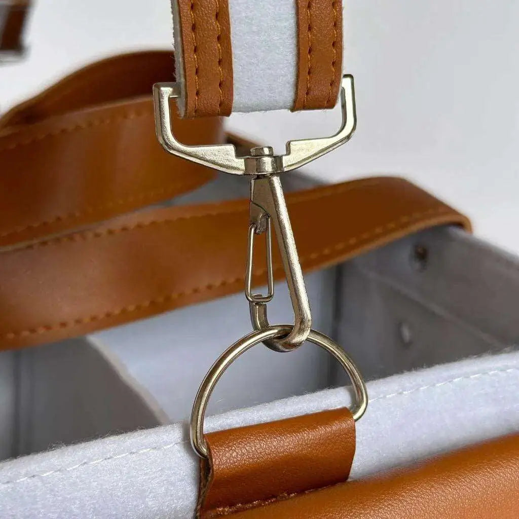 zoomed in view of silver hardware on a white with a hint of blue diaper caddy made of felt with leather accents