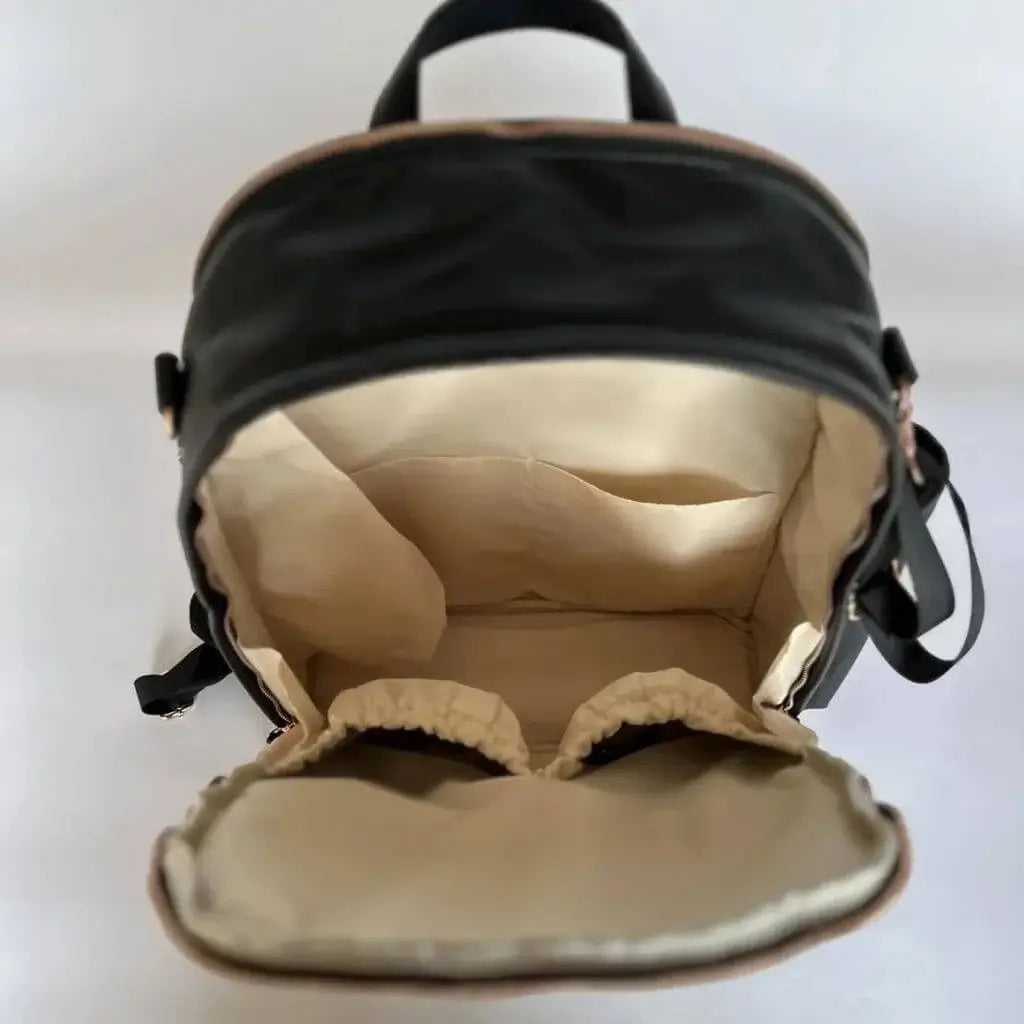 Overhead view of black leather backpack diaper bag with unzipped main compartment showing interior insulated pockets