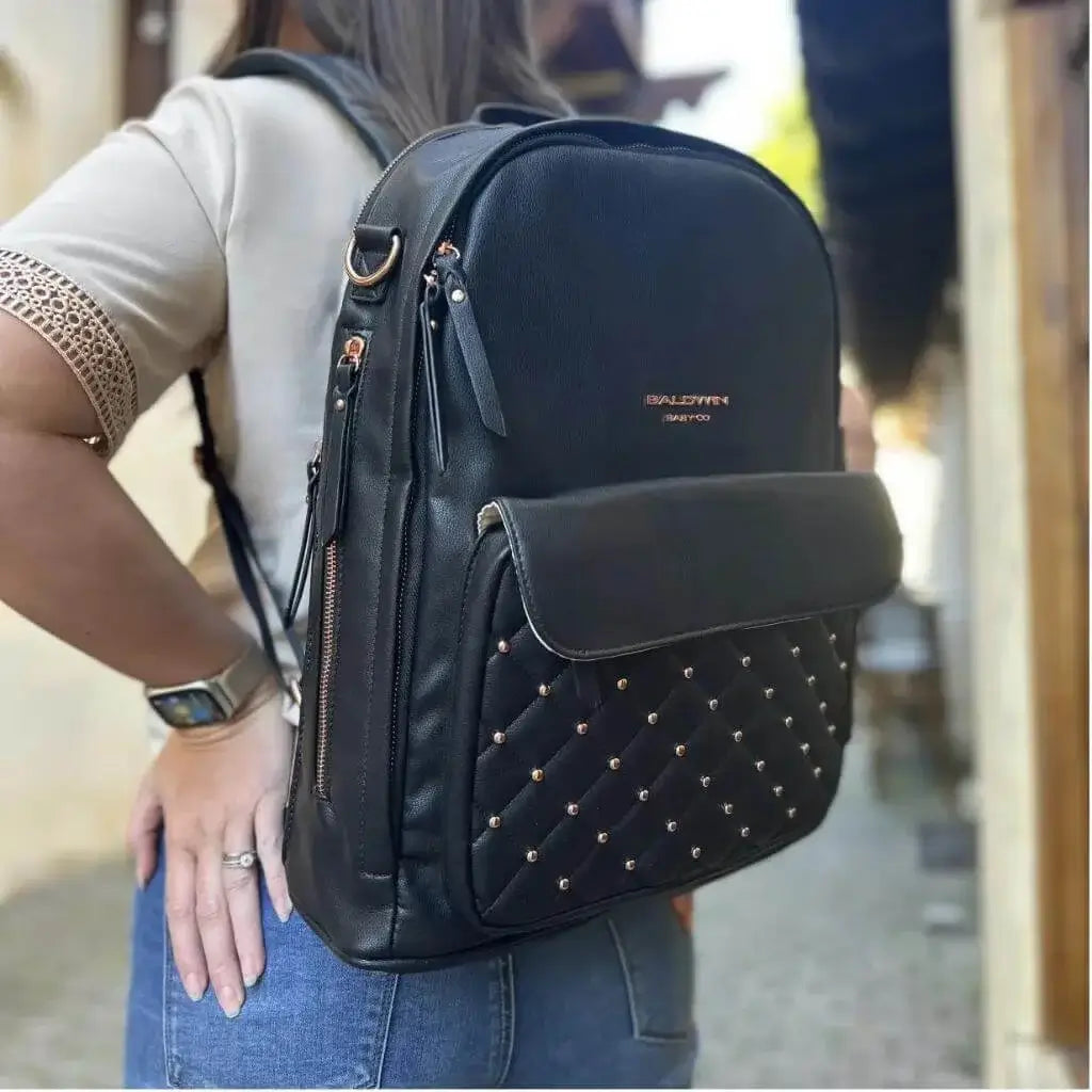 Woman wearing black leather backpack diaper bag with rose gold studs quilted on front pocket 
