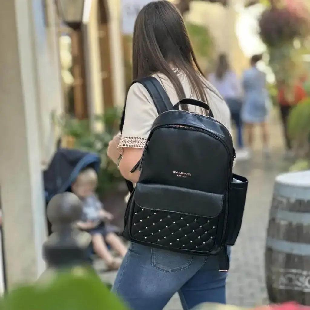 Woman walking with black leather backpack diaper bag with rose gold studs quilted on front pocket  