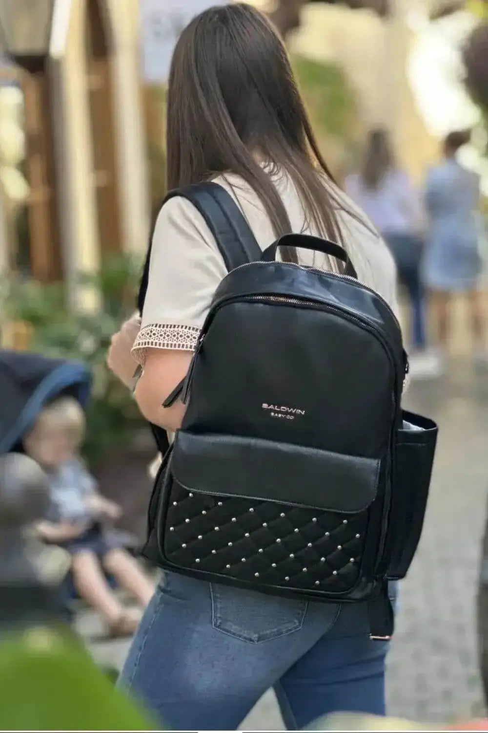 Woman walking with black leather backpack diaper bag with rose gold studs quilted on front pocket  