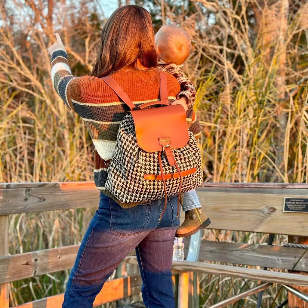 Woman holding a toddle on her hip while wearing a Houndstooth diaper bag drawstring backpack with leather details