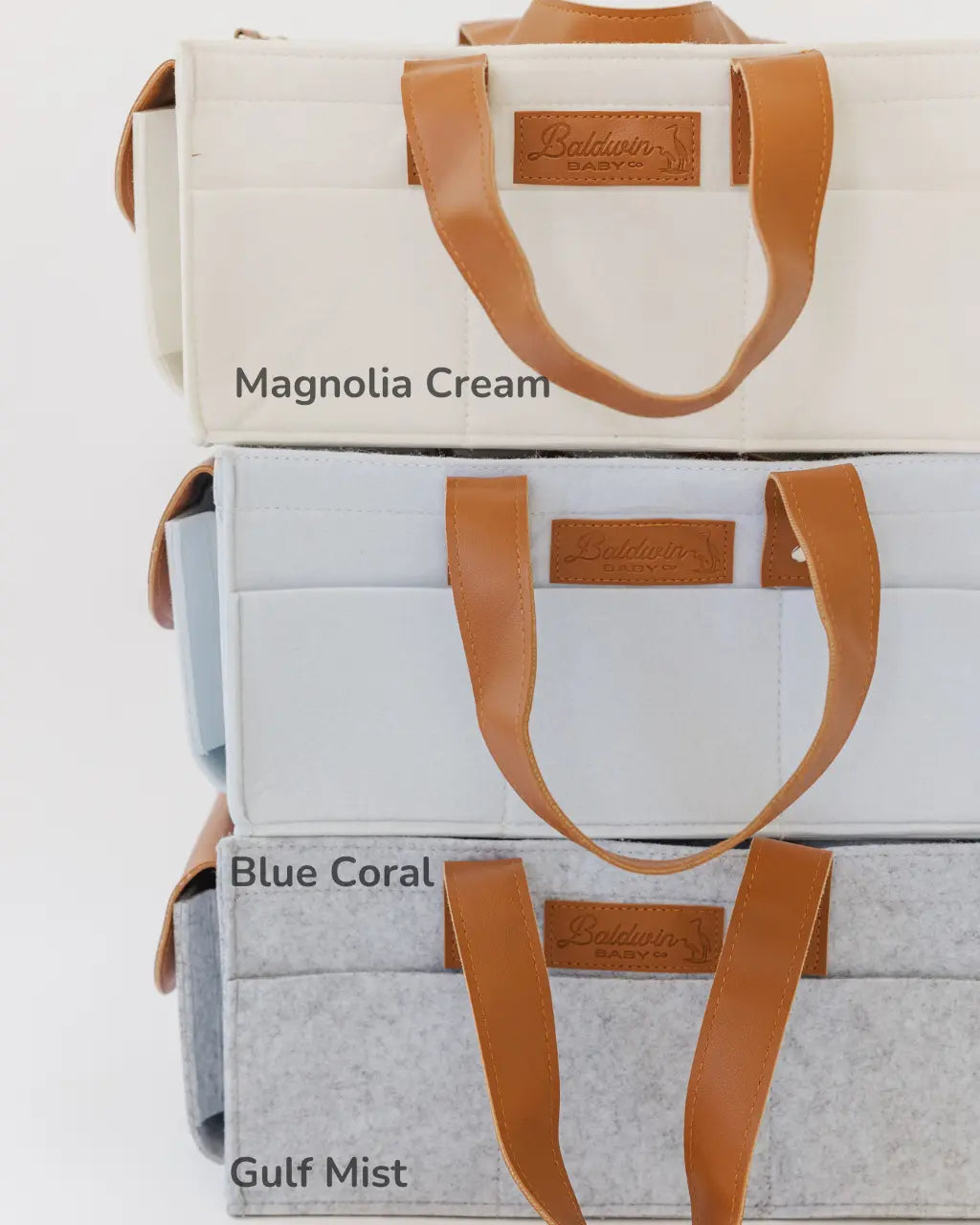 gray, blue, and white diaper caddies with brown leather handles stacked on top of each other