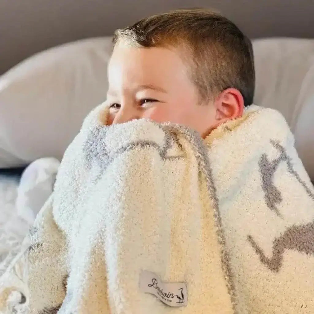 Young boy laughing and snuggled into a creamy white with a gray mother and baby heron silhouette pattern blanket