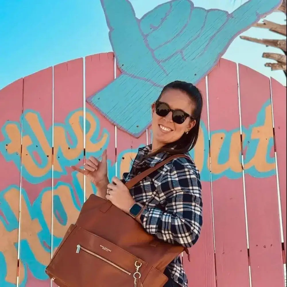 Woman in front of The Hangout sign wearing brown leather diaper bag by the shoulder straps