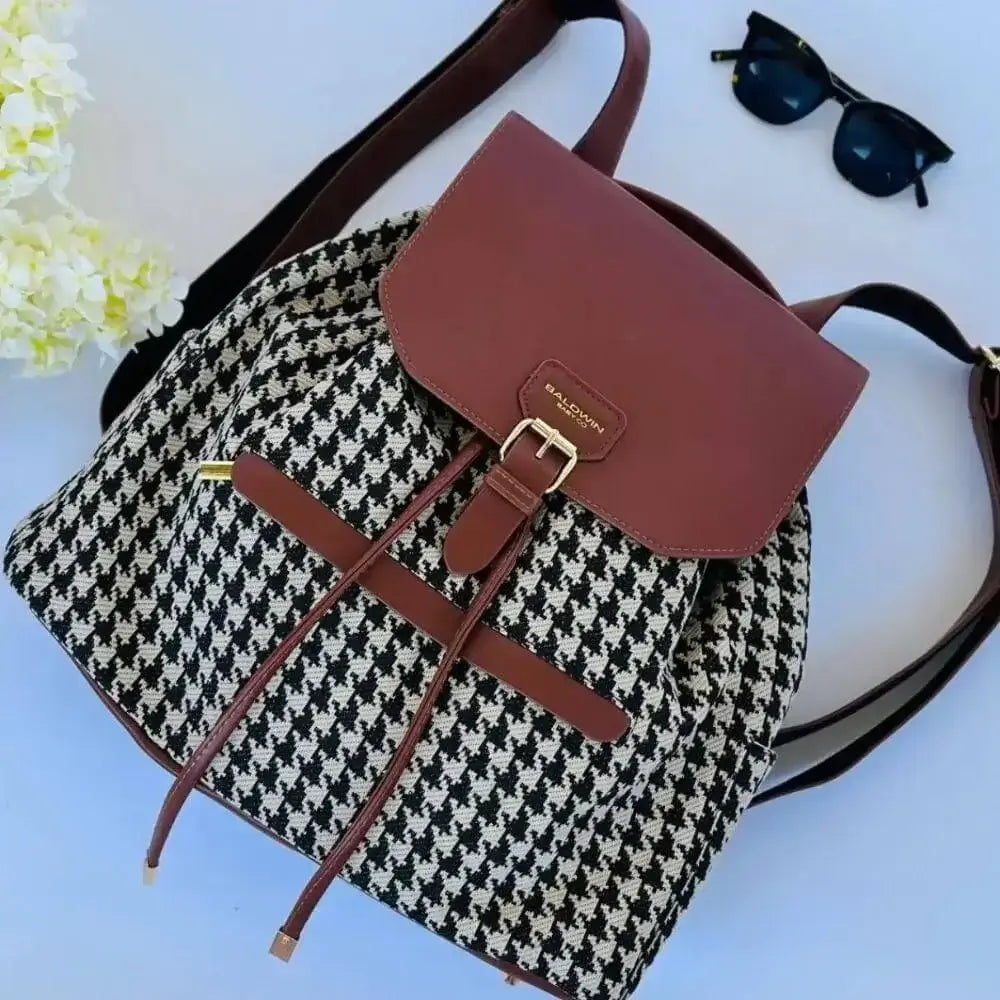 Houndstooth diaper bag drawstring backpack with leather details laid flat with flowers and sunglasses