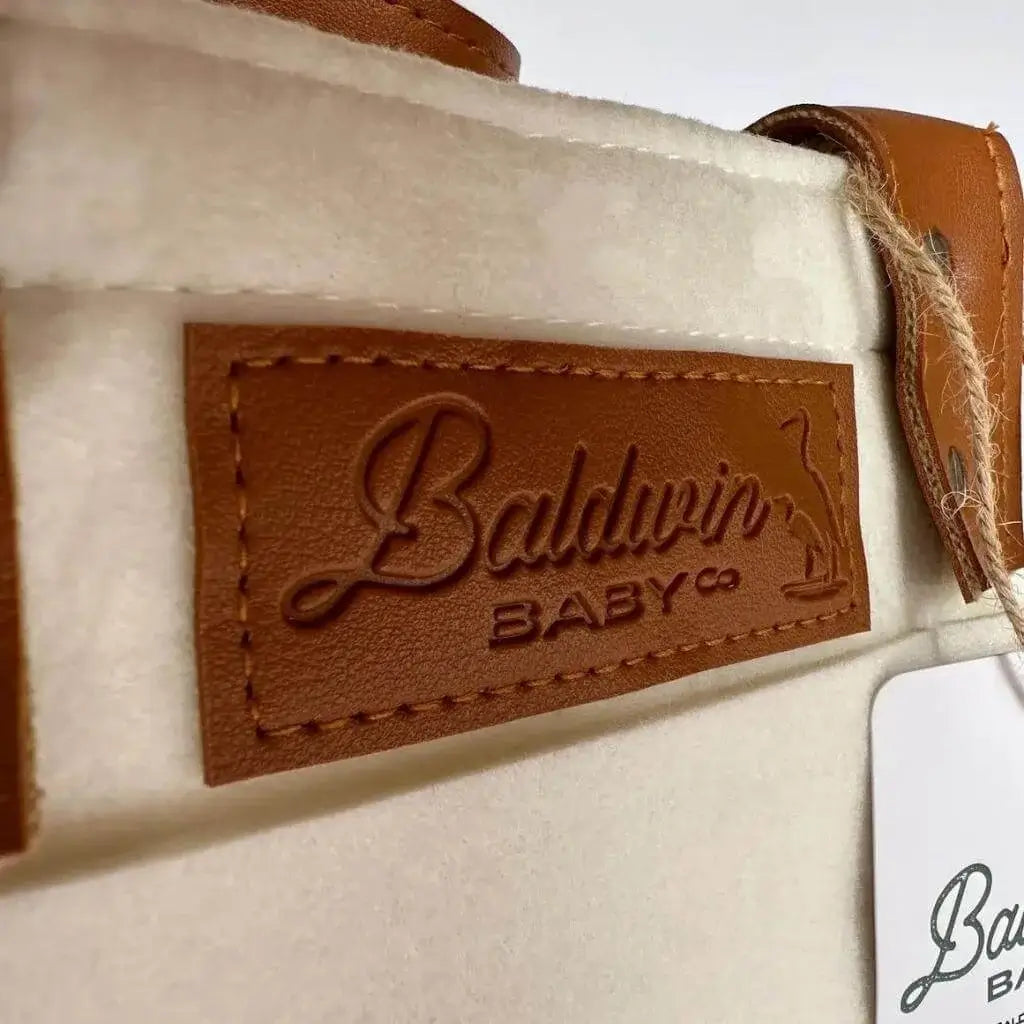 creamy white diaper caddy made of felt with the Baldwin Baby Company logo on leather accents 