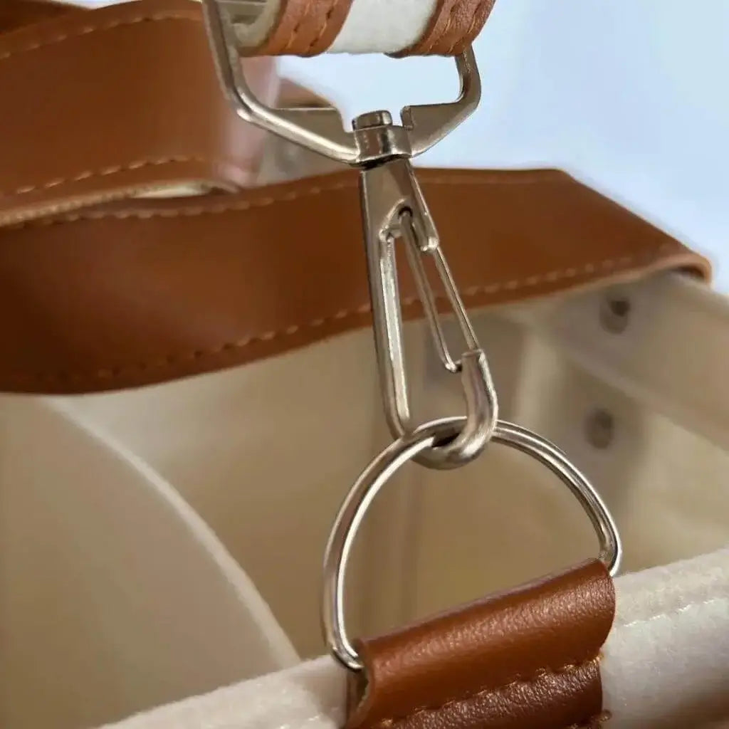 zoomed in view of silver hardware on a creamy white diaper caddy made of felt with leather accents