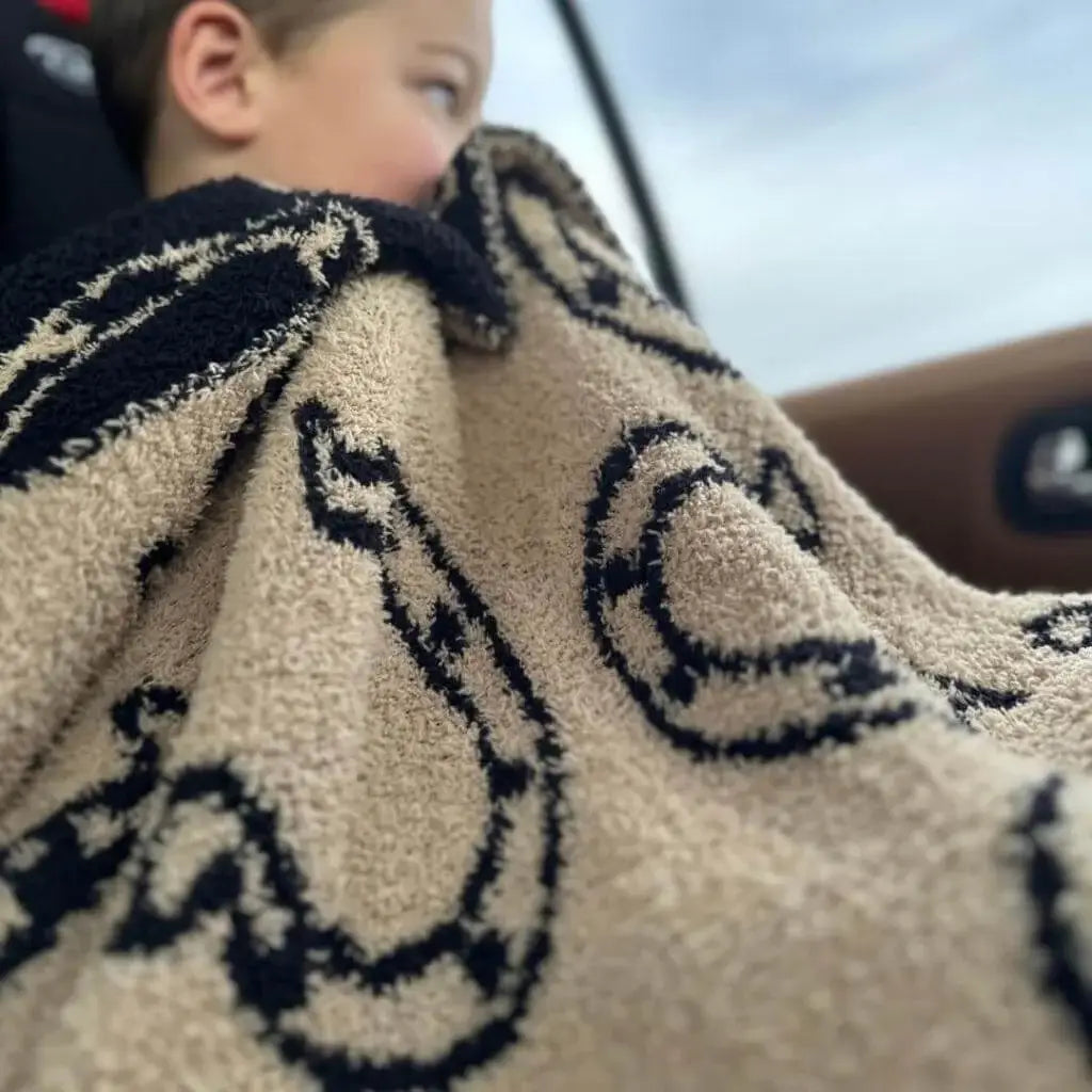 Tan with a black horseshoe pattern blanket laid in lap of child looking out a car window