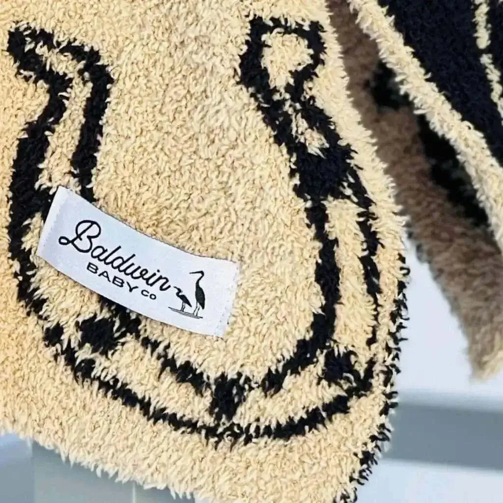 Close up of tan with a black horseshoe pattern fabric with a white Baldwin Baby Company logo tag