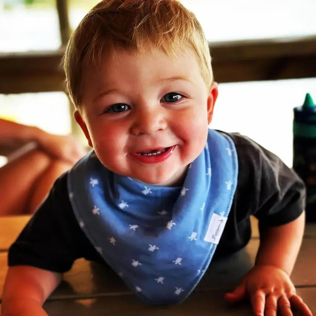 A smiling little boy wearing a blue bandana bib with a white sea turtle pattern