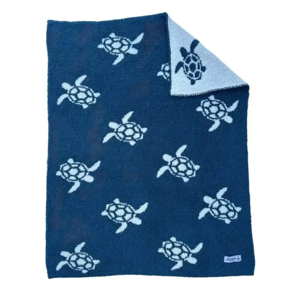 Blue with white sea turtle pattern blanket laid flat. A corner is folded over showing the other side has a reversed color pattern