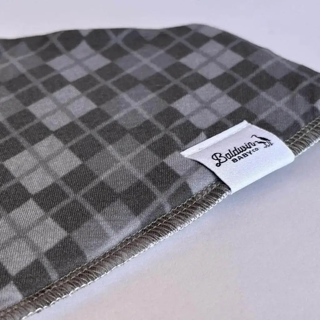 Close up of a grayscale plaid or argyle pattern bandana bib with a white Baldwin Baby Company logo tag