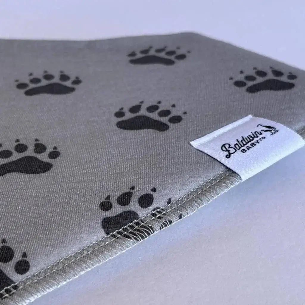 Close up of gray with black bear paw track pattern bandana bib with a white Baldwin Baby Company logo tag