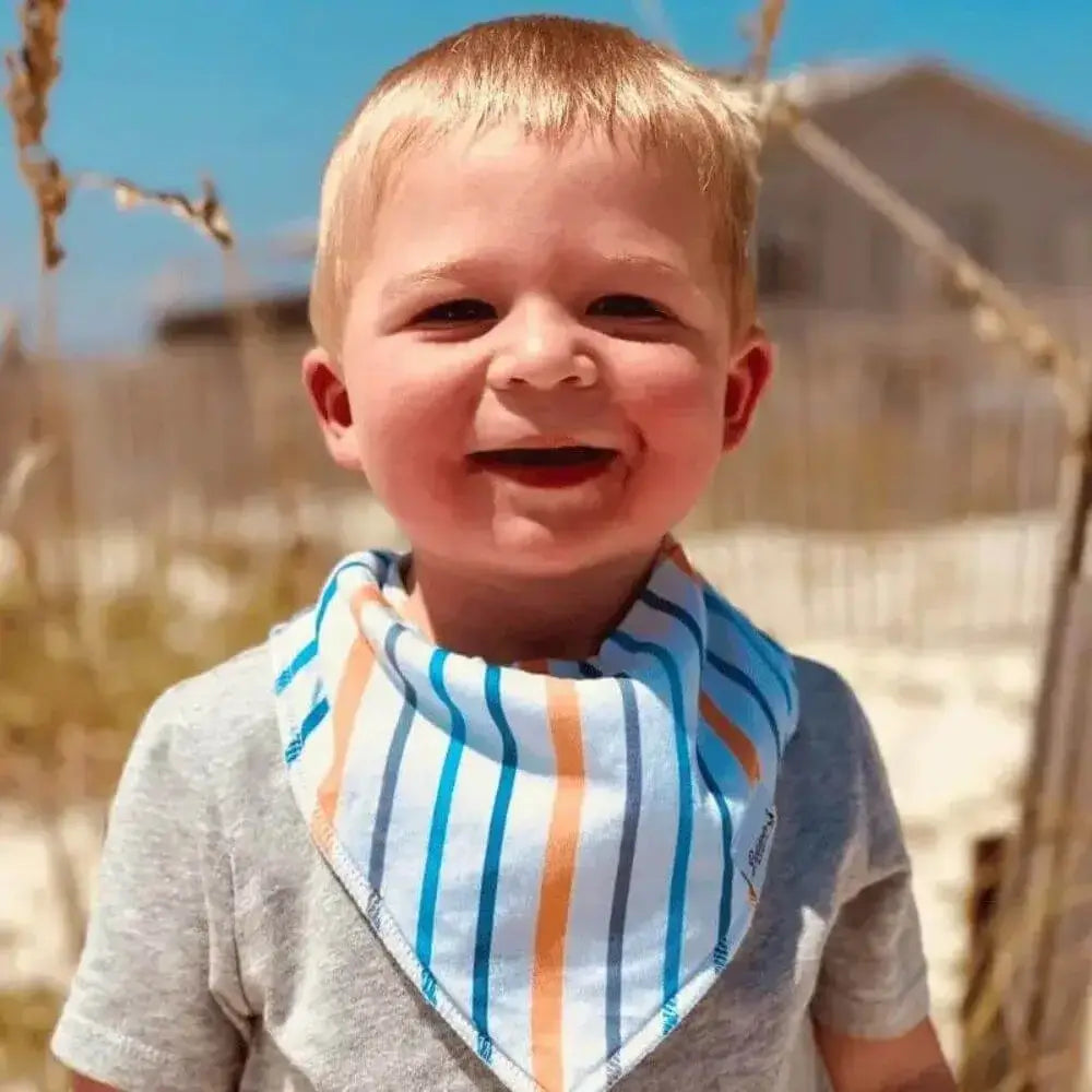 Little boy on the beach while wearing a white, blue, gray, and orange striped pattern bandana bib
