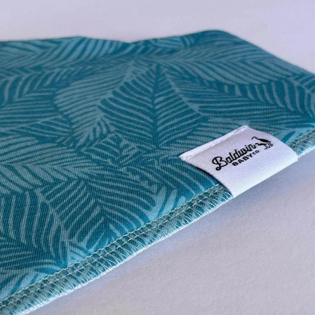 Close up of green monstera pattern bandana bib with a white Baldwin Baby Company logo tag